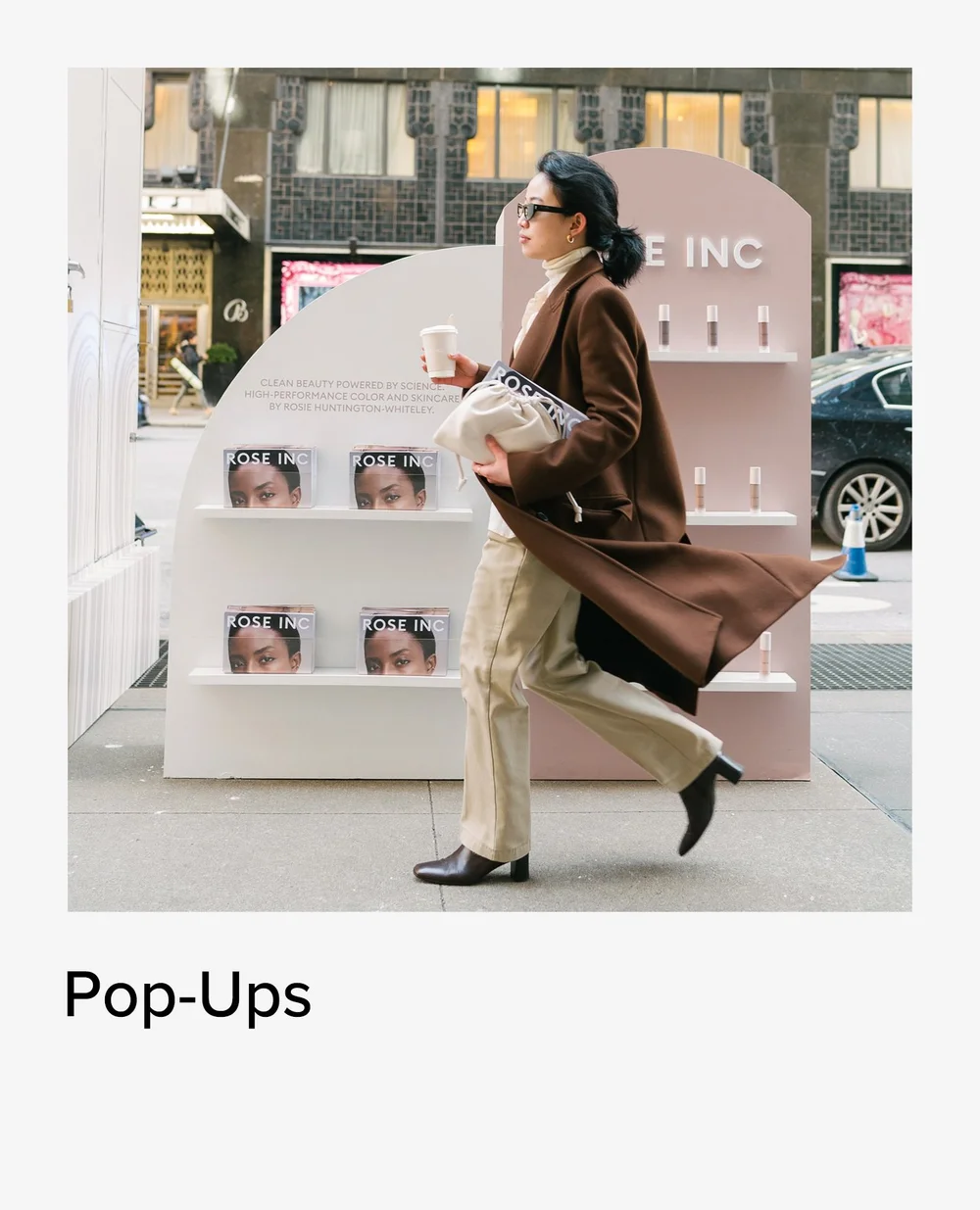 Woman walking past the Rose Inc pop-up in a brown coat, brand activation photography