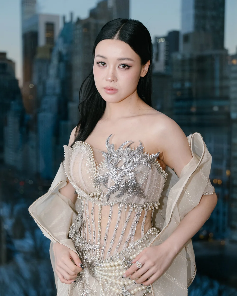 Emily Mei in a silver corset gown with the Manhattan skyline behind her