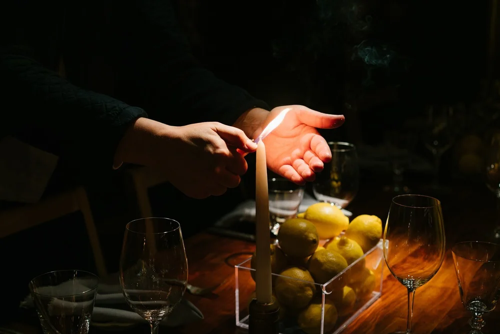 Candlelit table detail with hands and lemons at the Trinny London dinner, event photography