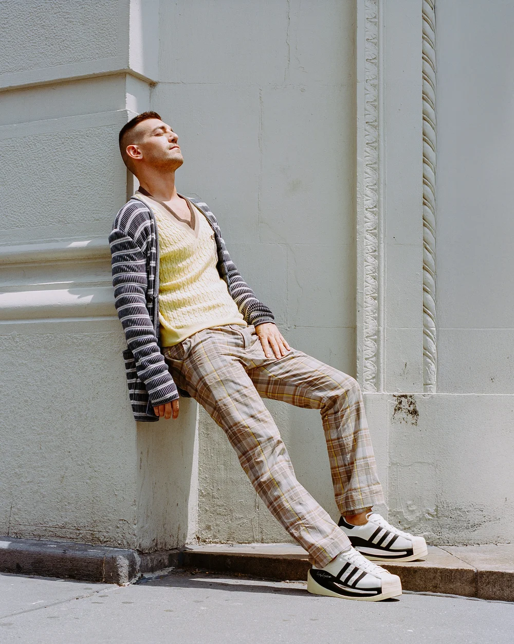 Matt Rogers in a striped cardigan leaning on a white column, ODDA editorial portrait