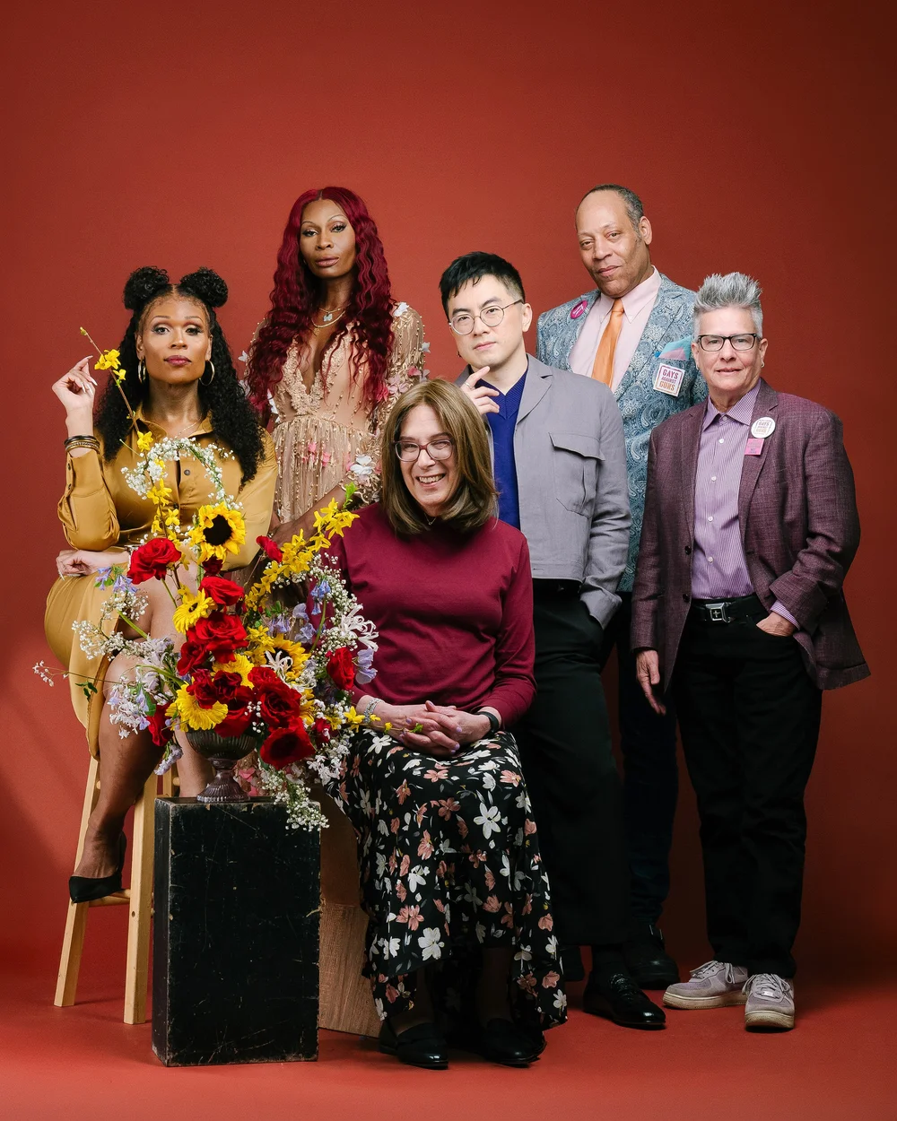 NYC Pride 2026 Grand Marshals group portrait with flowers against a red backdrop